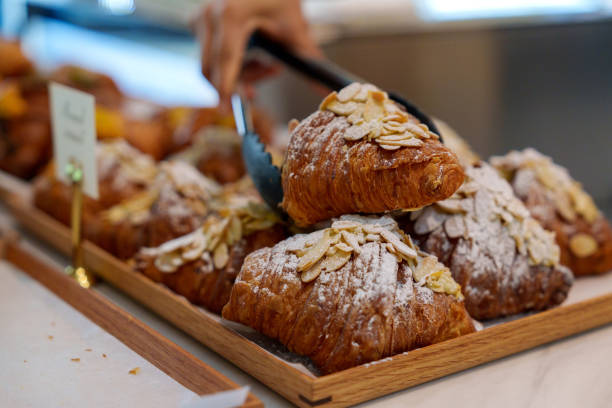 cropped image of an asian woman using tongs to pick up an almond croissant